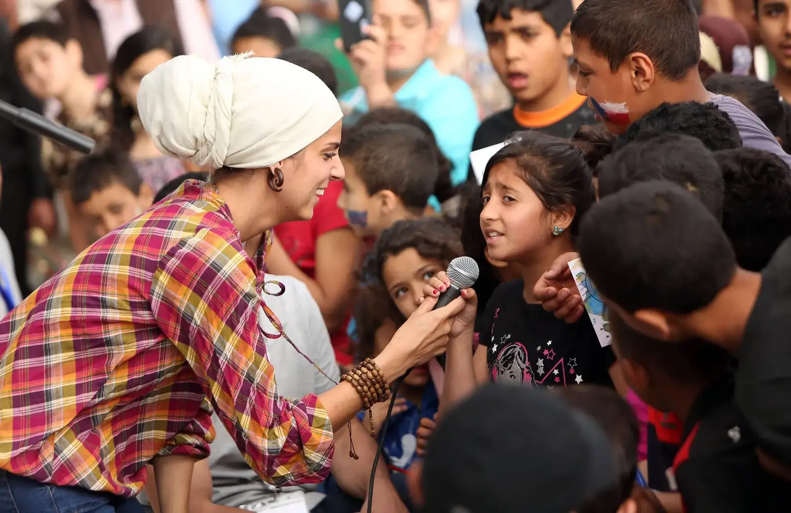 Rawan singing with a crowd of children around the microphone