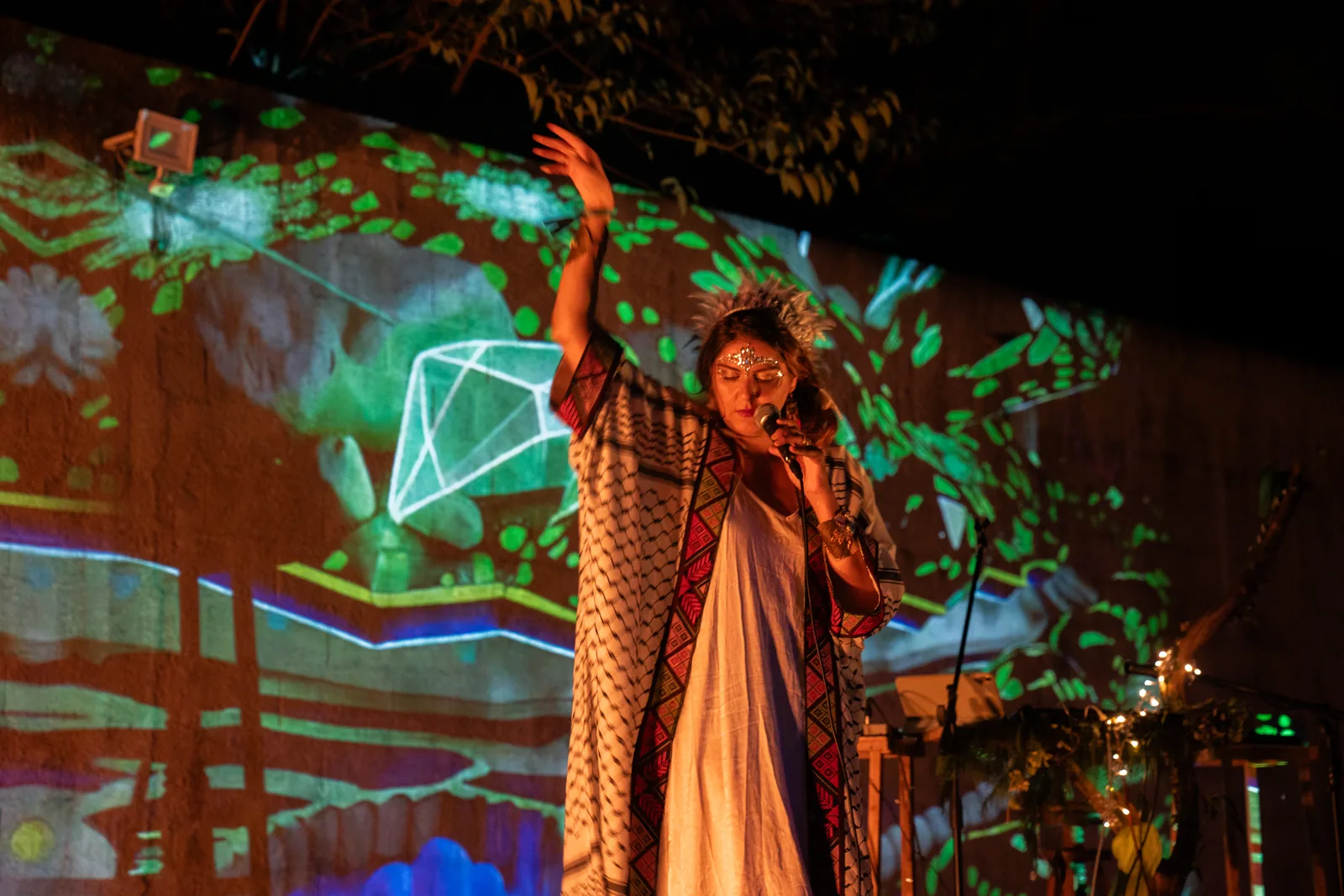 Rawan singing with one arm raised, geometric light projected across her